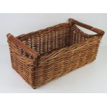 A wicker basket with wooden end handles.