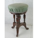 A Victorian piano stool raised over triform base and upholstered in green fabric.