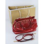 Michael Kors; a red patent handbag with original paper shopping bag and dust bag, approx 31cm wide.