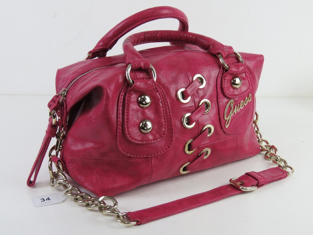 A hot pink handbag with shoulder strap by Guess, approx 30cm wide.