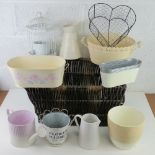 A wicker basket containing a quantity of assorted planters, jugs, watering cans, etc.