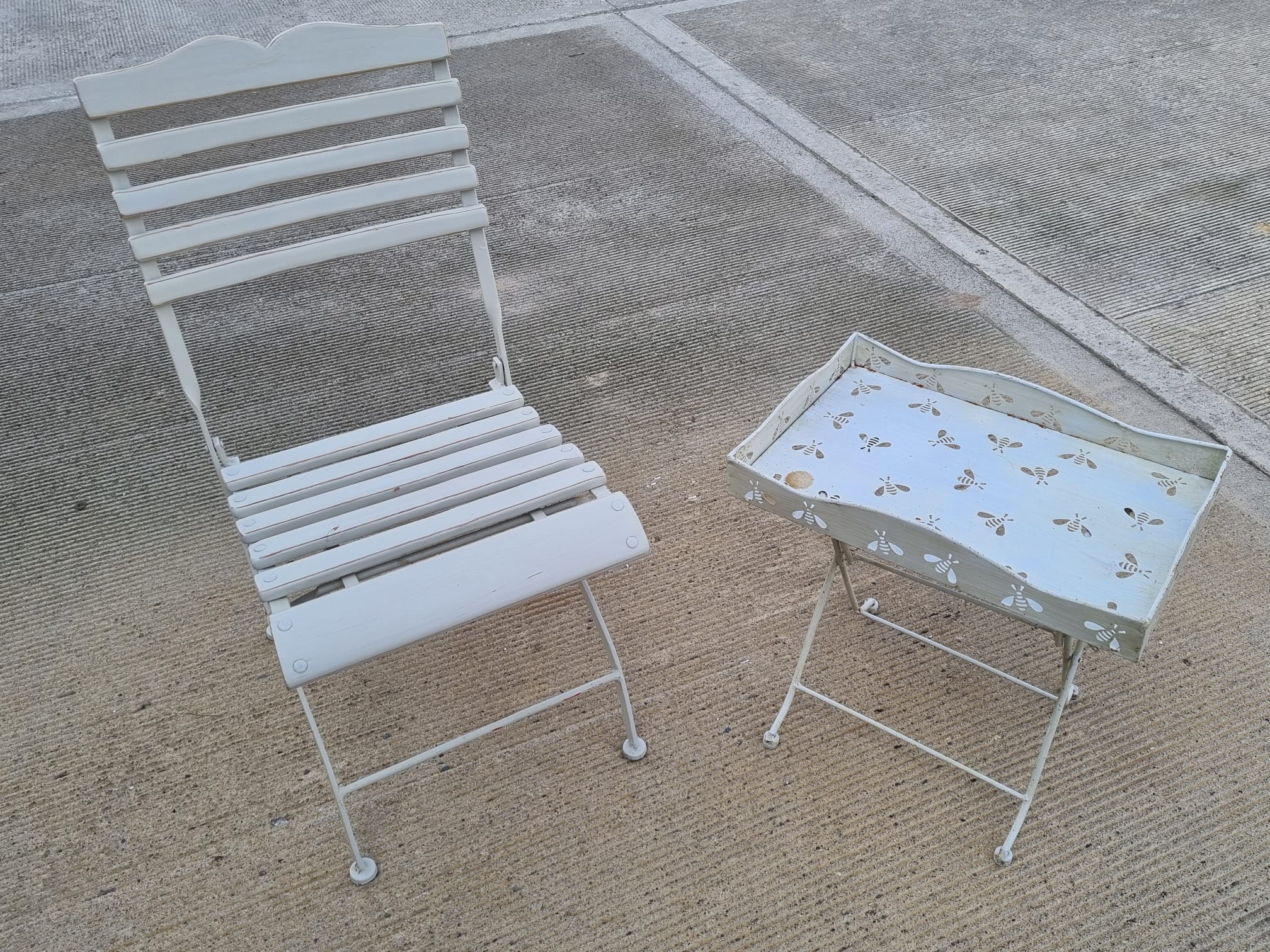 A single white bistro chair with white metal table having bee pattern.