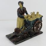 A traditionally dressed Welsh lady stood next to cart with cream coloured churns upon,