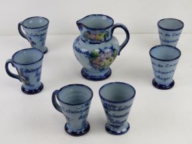 A hand painted c1962 themed jug and cup set in blue glaze having floral decoration upon.