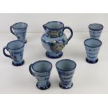 A hand painted c1962 themed jug and cup set in blue glaze having floral decoration upon.