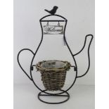 A teashop sign having wicker planter within black metal 'teapot' frame with Welcome sign over,