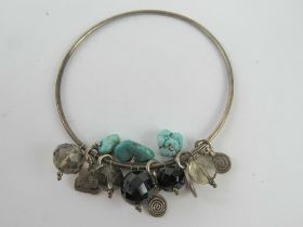 A white metal bangle having turquoise and quartz beads upon.