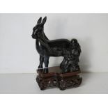A carved serpentine Oriental figurine of a man with donkey, a/f, raised over carved hard wood base.