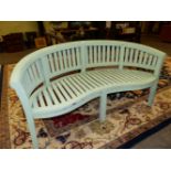 A GREEN PAINTED GARDEN BENCH, THE CURVED TOP RAIL ABOVE A SLATTED BACK AND SEAT ON SIX SQUARE SECTI