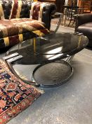 AN ART DECO BLACK GLASS OVAL TOPPED COFFEE TABLE, THE TOP SUPPORTED BY PAIRS OF CHROME STRAP LEGS