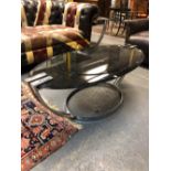AN ART DECO BLACK GLASS OVAL TOPPED COFFEE TABLE, THE TOP SUPPORTED BY PAIRS OF CHROME STRAP LEGS