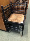 AN ARTS AND CRAFTS EBONISED CORNER DESK CHAIR IN GODWIN STYLE, THE RUSH SEAT ABOVE TURNED