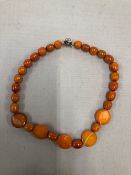 A GRADUATED BEADED AMBER NECKLACE FITTED WITH A RHINESTONE SET CLASP. LENGTH APPROX 43cms WEIGHT