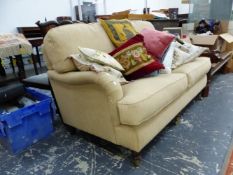 AN OATMEAL UPHOLSTERED TWO SEAT SETTEE ON MAHOGANY LEGS WITH BRASS CASTER FEET. W 157cms.