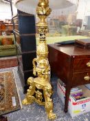 A CARVED GILT AND EBONISED STANDARD LAMP WORKED WITH MASKS AND FOLIAGE ABOVE THREE PAW FEET, THE