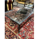 A GLASS TOPPED IRON COFFEE TABLE WITH SCROLLING FOLIAGE BELOW THE TOP AND ON LEGS OF THREE SQUARE