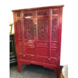 A CHINESE RED PAINTED CABINET, THE DOORS AND SIDES PIERCED WITH SCROLLING FOLIAGE AND CARVED
