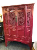 A CHINESE RED PAINTED CABINET, THE DOORS AND SIDES PIERCED WITH SCROLLING FOLIAGE AND CARVED