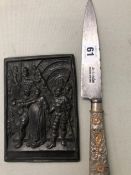 AN ANTIQUE WHITE METAL CHASED HANDLE ARGENTINIAN KNIFE TOGETHER WITH A BRONZE RELIEF CASTED PLAQUE.