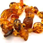 A ROW OF IRREGULAR SHAPED AMBER BEADS WITH A SCREW FITTING CLASP. LENGTH 56cms. WEIGHT 76grms.