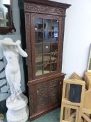 AN ANTIQUE CARVED OAK FLOOR STANDING TWO PART CORNER CABINET WITH GLAZED UPPER DOOR.