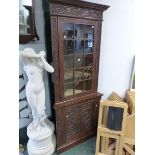 AN ANTIQUE CARVED OAK FLOOR STANDING TWO PART CORNER CABINET WITH GLAZED UPPER DOOR.