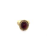 AN ANTIQUE GARNET AND DIAMOND CLUSTER RING. THE CENTRAL OVAL CABOCHON, SURROUNDED BY A CLUSTER OF