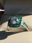 A DIAMOND AND EMERALD ART DECO STYLE RING, THE CENTRAL DIAMOND SURROUNDED BY A HALO OF FANCY CUT