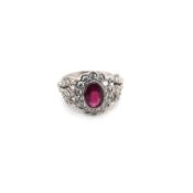 A PLATINUM HALLMARKED RUBY AND DIAMOND CLUSTER RING WITH DIAMOND SET FOLIATE STYLE SHOULDERS. FINGER