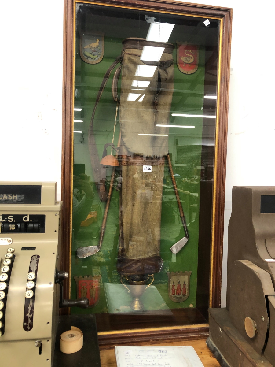 A FRAMED GOLF BAG ARRANGED WITH TWO IRON CLUBS WITHIN FOUR ARMORIAL SHIELDS, THE FRAME. 90 x 58.