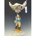 A JOHN BEVINGTON FIGURAL TABLE CENTREPIECE, THE TWO HANDLED FLOWER ENCRUSTED BASKET ABOVE A MAN