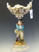 A JOHN BEVINGTON FIGURAL TABLE CENTREPIECE, THE TWO HANDLED FLOWER ENCRUSTED BASKET ABOVE A MAN