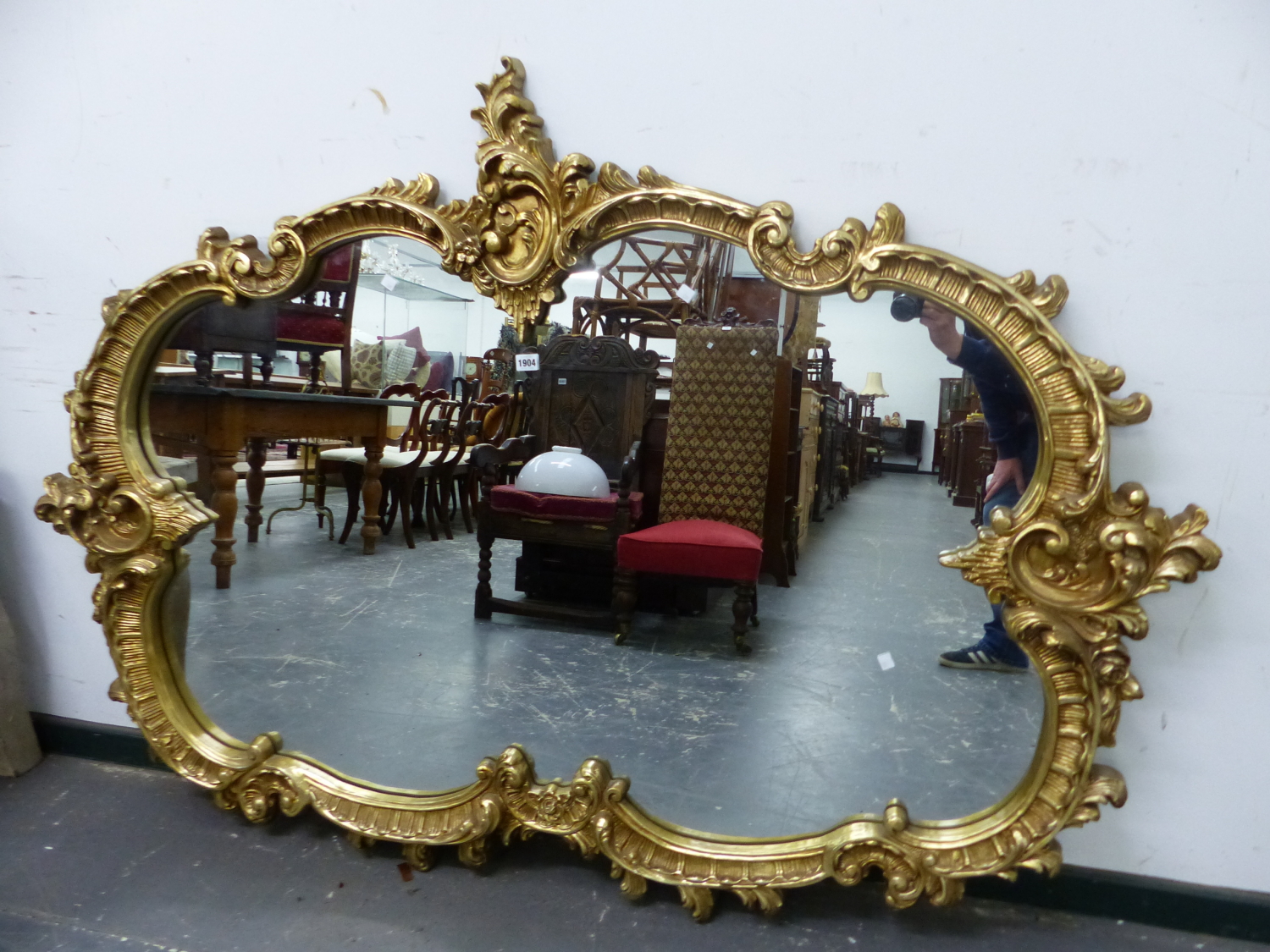 A 20th C. OVAL MIRROR IN A GILT COMPOSITION FRAME MOULDED WITH ROCAILLE AND FOLIAGE. W 178 x