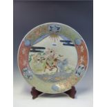 A JAPANESE IMARI DISH WITH A WOOD STAND, THE CENTRE PAINTRED WITH A HORSEMAN AND ATTENDANTS