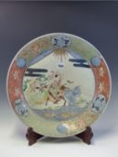 A JAPANESE IMARI DISH WITH A WOOD STAND, THE CENTRE PAINTRED WITH A HORSEMAN AND ATTENDANTS