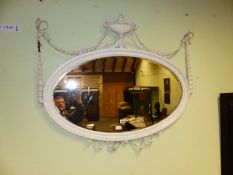 A VICTORIAN BEVELLED GLASS OVAL MIRROR, THE WHITE PAINTED FRAME SURMOUNTED BY AN URN AND RIBBON TIED