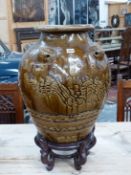 A MARTABAN BROWN GLAZED STONEWARE STORAGE JAR AND WOOD STAND, THE OVOID BODY WITH FIVE LIONS HEADS