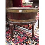 A GEORGE III BRASS COOPERED TWO HANDLED OVAL WINE COOLER RAISED ON FOUR CANTED LEGS ON CASTER