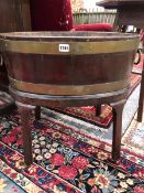 A GEORGE III BRASS COOPERED TWO HANDLED OVAL WINE COOLER RAISED ON FOUR CANTED LEGS ON CASTER