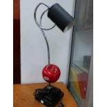 A NOVELTY TABLE LAMP, THE BLACK TIN CAN STYLE SHADE ON A COILED CHROME ARM PIERCING A RED APPLE