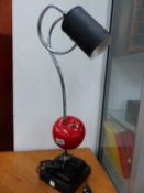 A NOVELTY TABLE LAMP, THE BLACK TIN CAN STYLE SHADE ON A COILED CHROME ARM PIERCING A RED APPLE