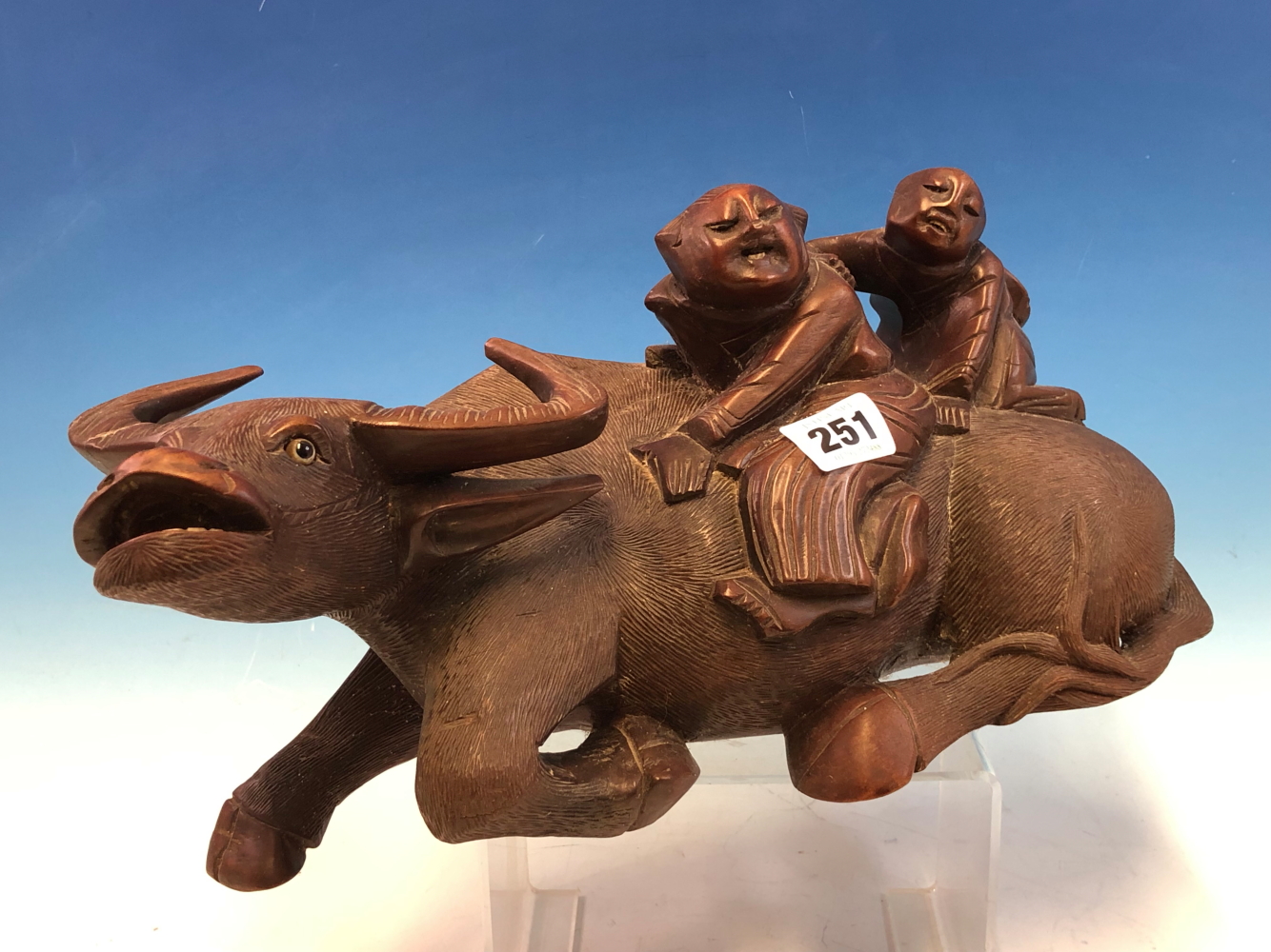 A CHINESE HARDWOOD CARVING OF TWO CHILDREN ON THE BACK OF A GLASS EYED RECLINING BUFFALO. W 33cms.