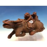 A CHINESE HARDWOOD CARVING OF TWO CHILDREN ON THE BACK OF A GLASS EYED RECLINING BUFFALO. W 33cms.