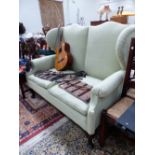 A GREEN UPHOLSTERED TWO SEAT WING SETTEE ON MAHOGANY CABRIOLE LEGS WITH CLUB FEET. W 154 x D 80 x