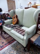 A GREEN UPHOLSTERED TWO SEAT WING SETTEE ON MAHOGANY CABRIOLE LEGS WITH CLUB FEET. W 154 x D 80 x