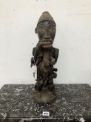 AN IVORY COAST MAHOGANY FETISH, THE LADEN FIGURE STANDING WITH HIS RIGHT HAND BETWEEN HIS TEETH,