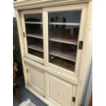 A WHITE PAINTED PINE KITCHEN CABINET, THE GLAZED DOORS TO THE UPPER HALF SLIDING OVER SHELVES AND