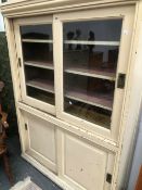 A WHITE PAINTED PINE KITCHEN CABINET, THE GLAZED DOORS TO THE UPPER HALF SLIDING OVER SHELVES AND
