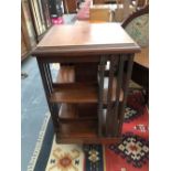 AN EDWARDIAN MAHOGANY ROTARY BOOK CASE, THE CRUCIFORM LEGS ON CASTER FEET. H 90cms W 49cms D 49cm