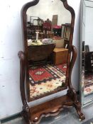 A VICTORIAN MAHOGANY FULL LENGTH CHEVAL MIRROR, THE WAVY PLINTH ABOVE SCROLL FRONT LEGS ON CASTER